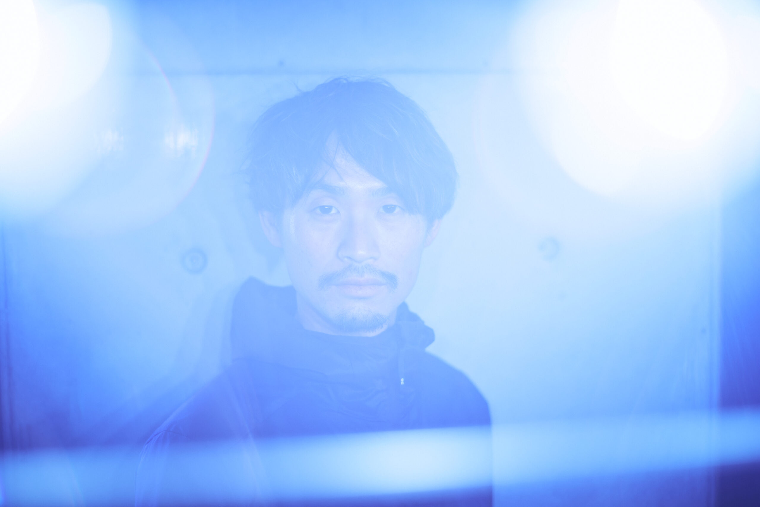 青い逆光の中こちらを見つめている横田さんの写真