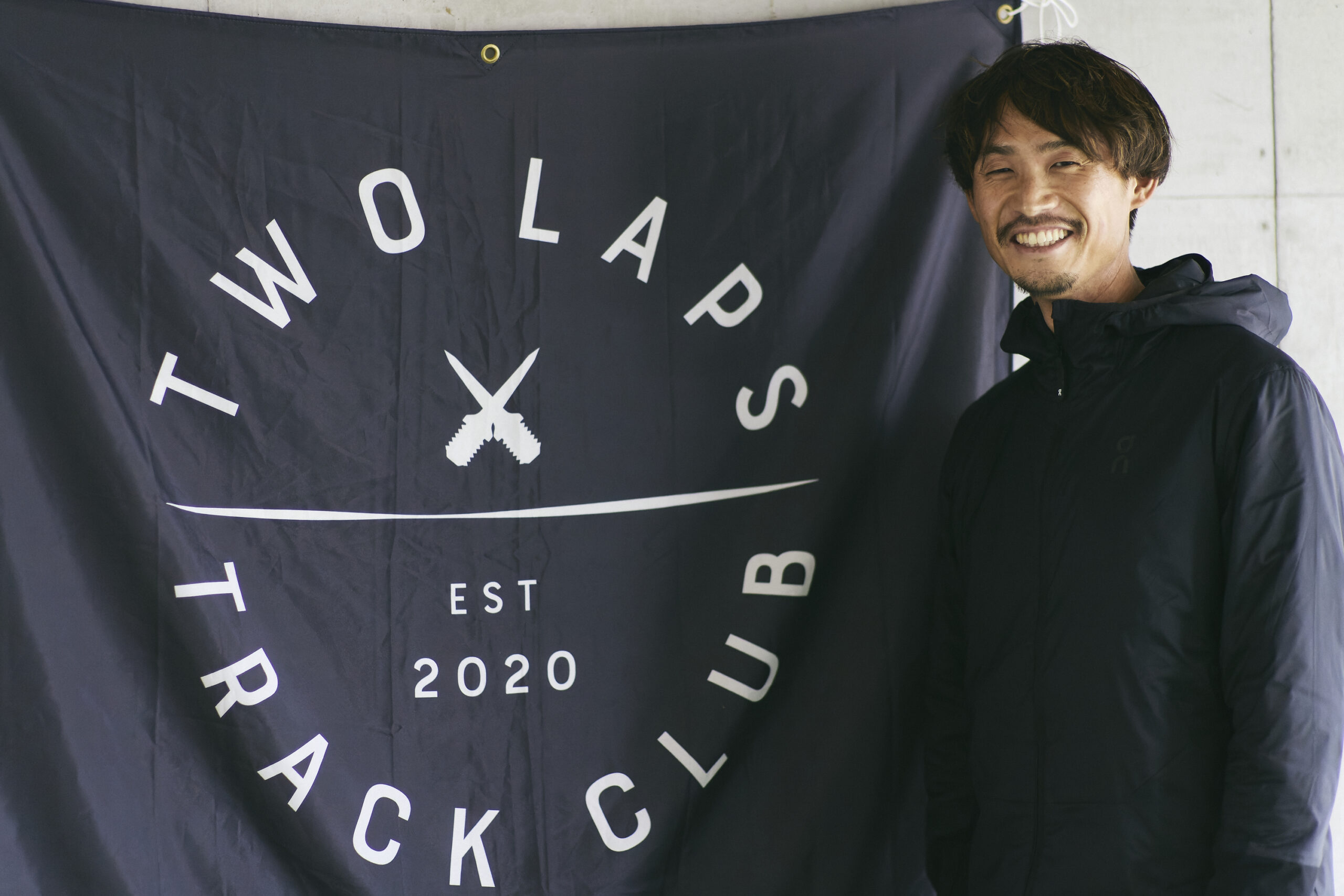 TWOLAPSのは旗の前で立つ横田さんの写真