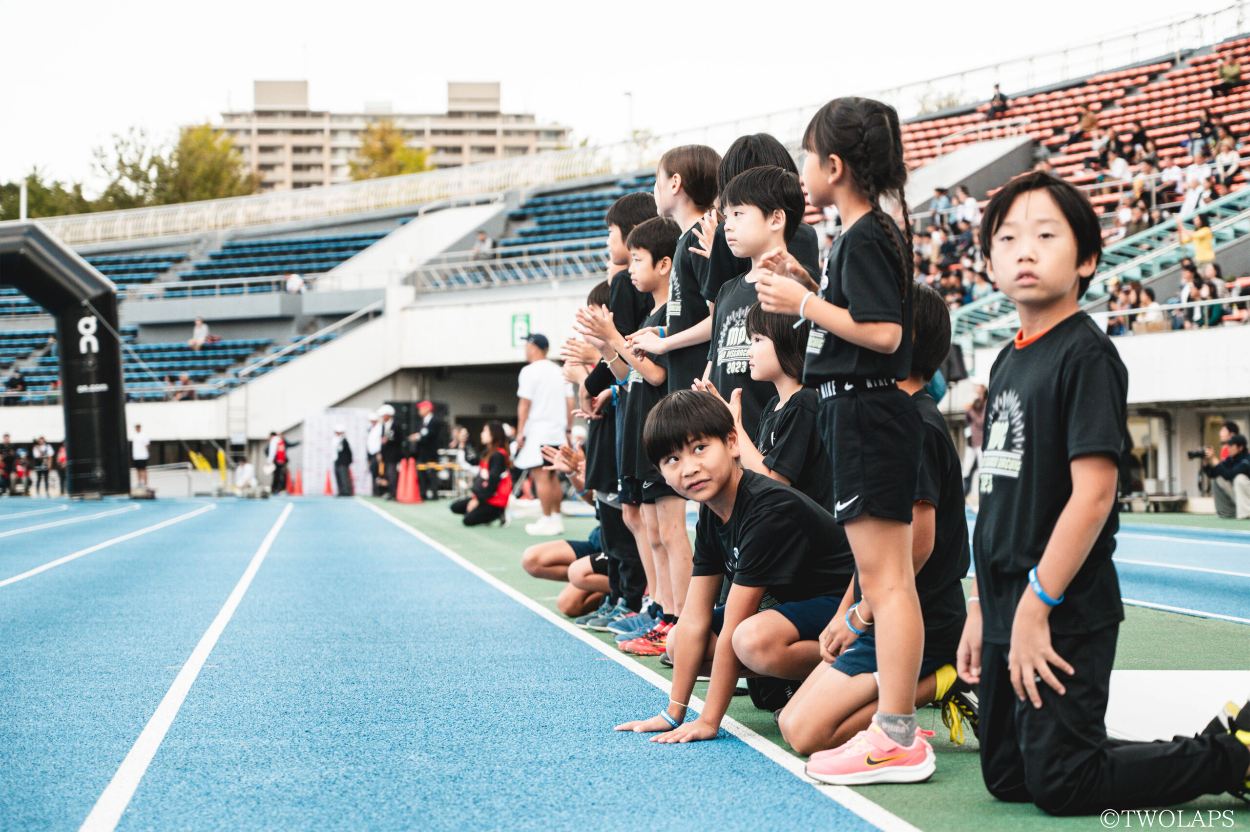 陸上競技場で選手を見ている子どもたちの写真
