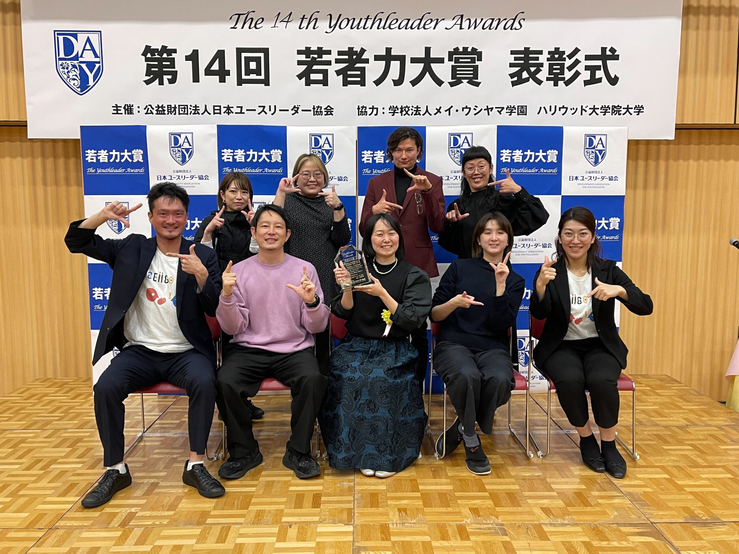 第14回若者力大賞表彰式のパネル前で受賞者と一緒に写る菊永さんの写真