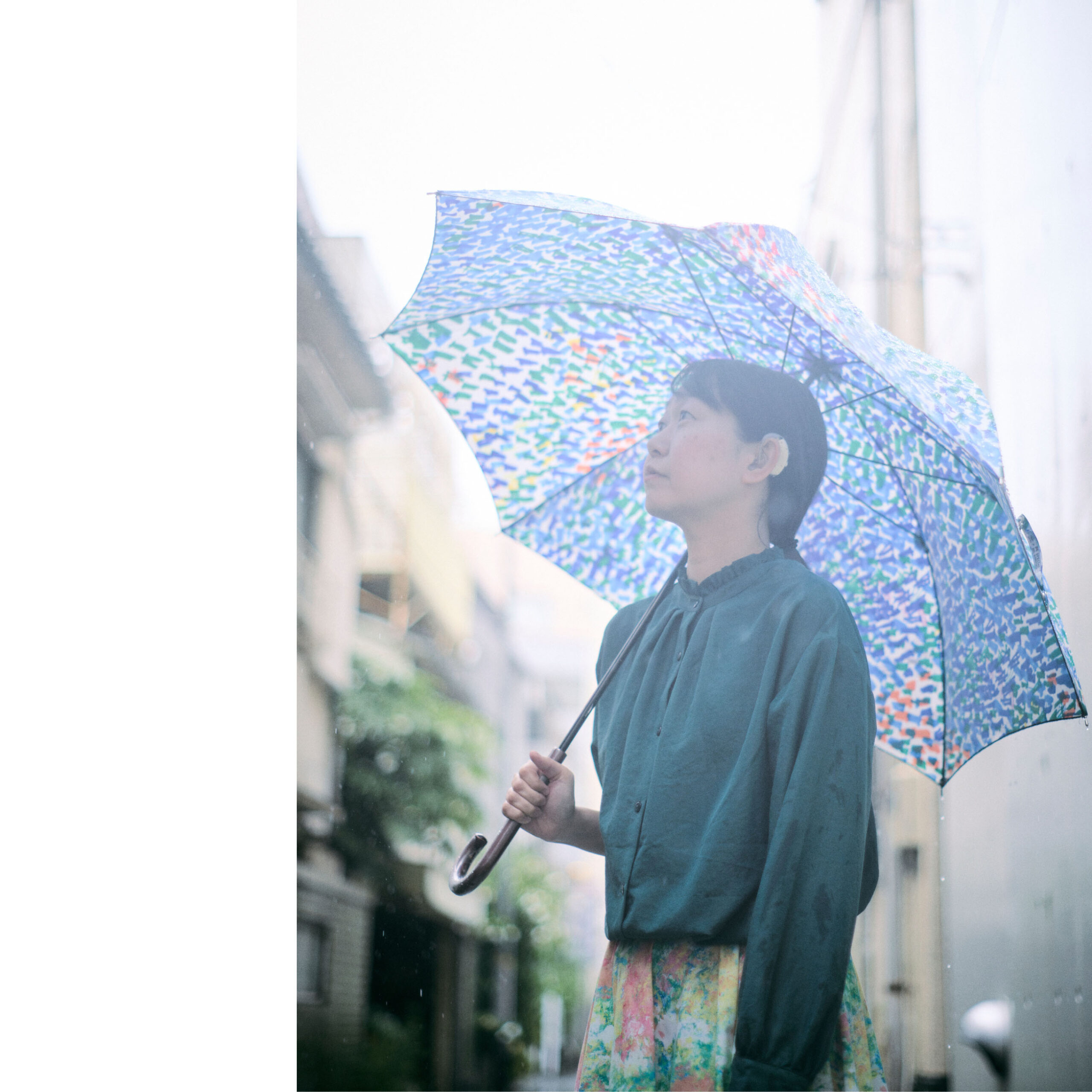 路地裏で傘をさしながら斜め上をみつめている菊永さんの写真