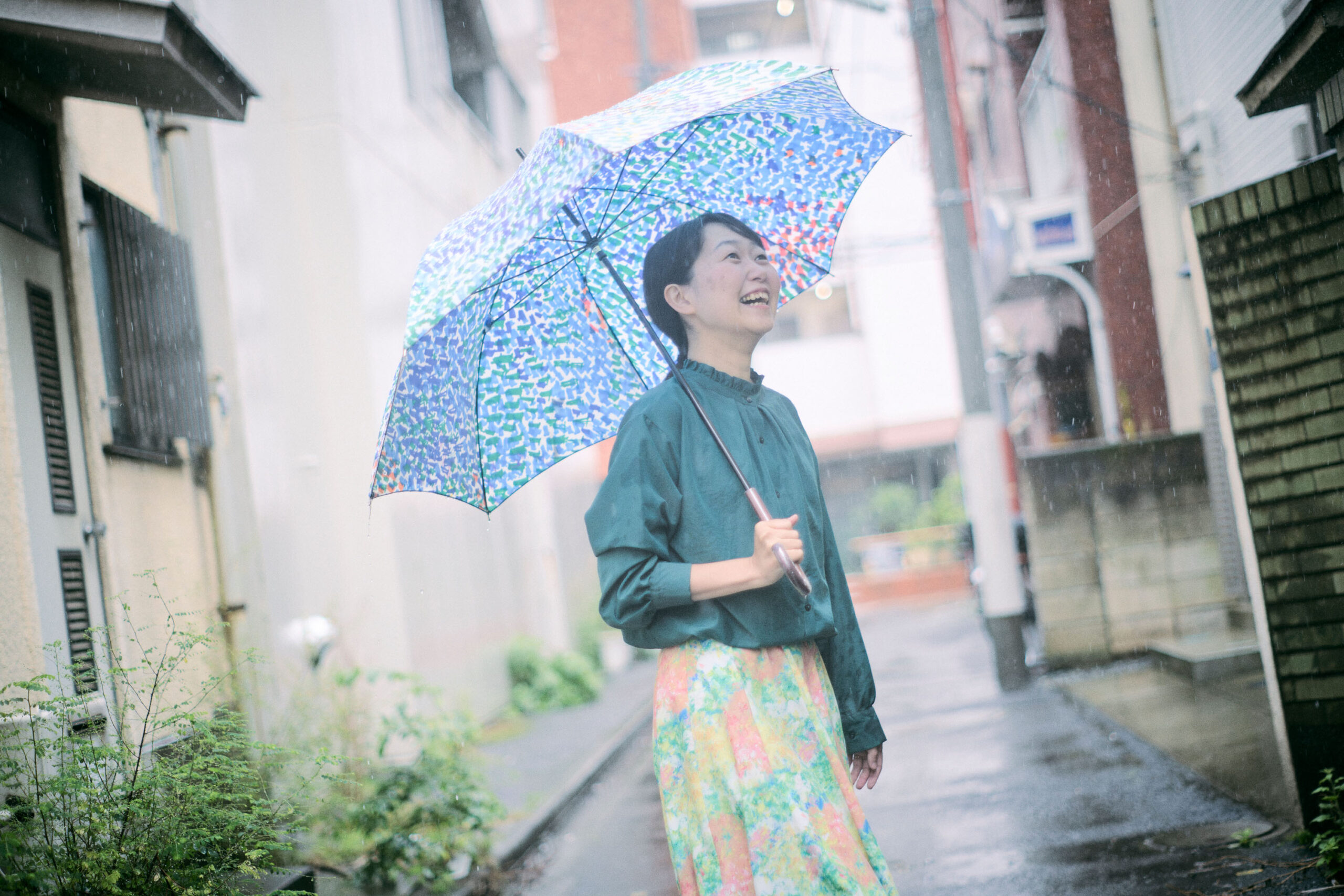 路地裏で傘を指して微笑んでいる菊永さんの写真