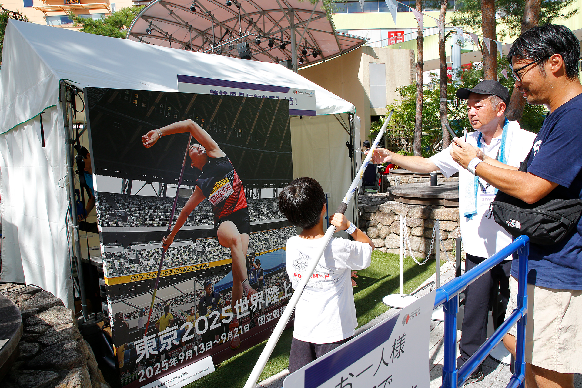 北口選手のパネル前でやり投げの棒を持っている男の子の写真