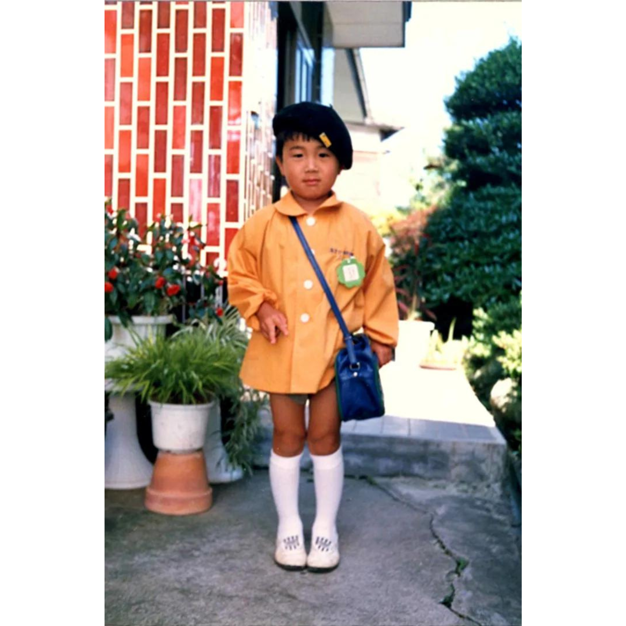 幼稚園のスモッグを着て家の前で撮られた五十嵐さんの写真