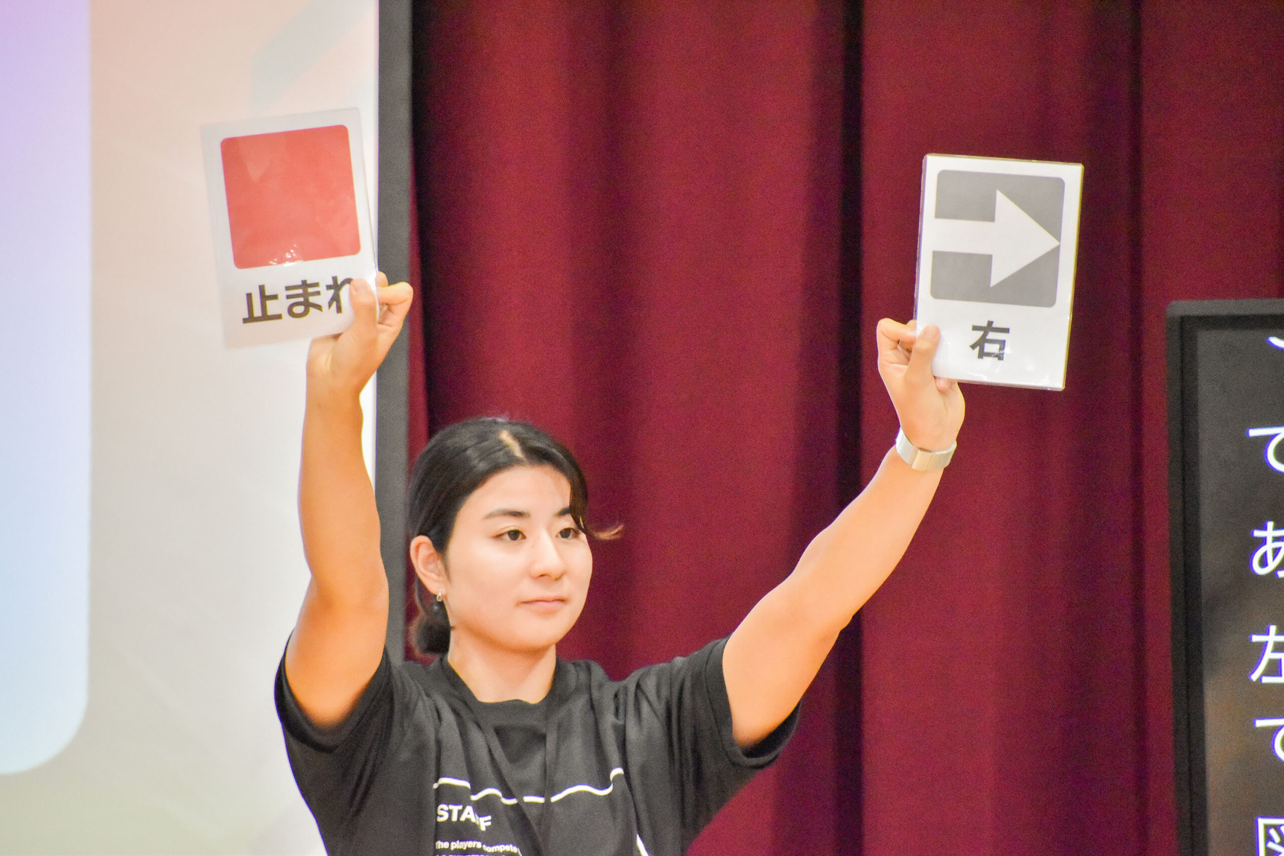 右手に赤い四角と止まれと書かれた紙を持ち、左手に右矢印と右と書かれた紙を持っている女性の写真