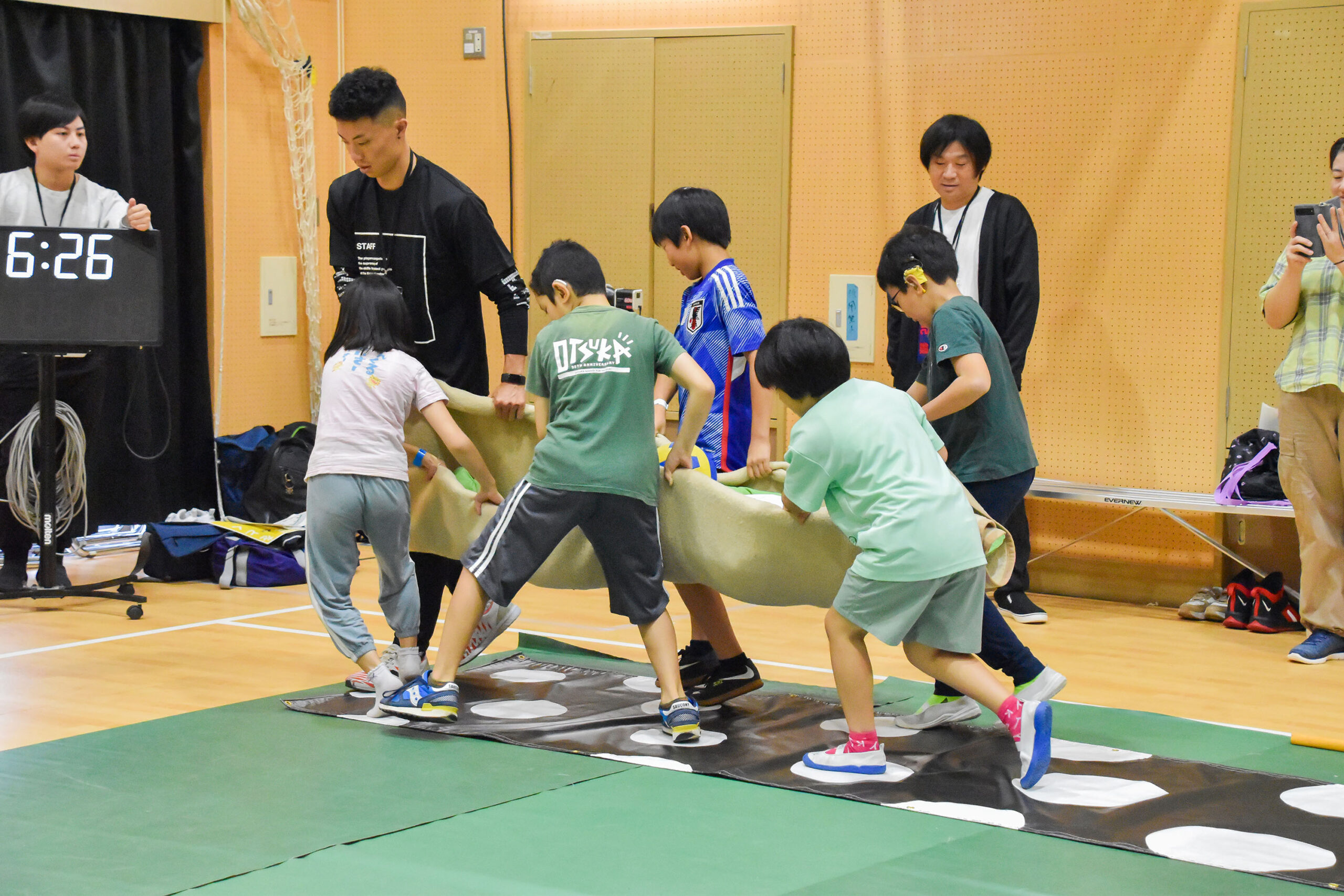 床に白黒の水玉模様のシートが敷いてあり、白い部分だけを歩きながら毛布のぬいぐるみを運んでいる参加者の写真