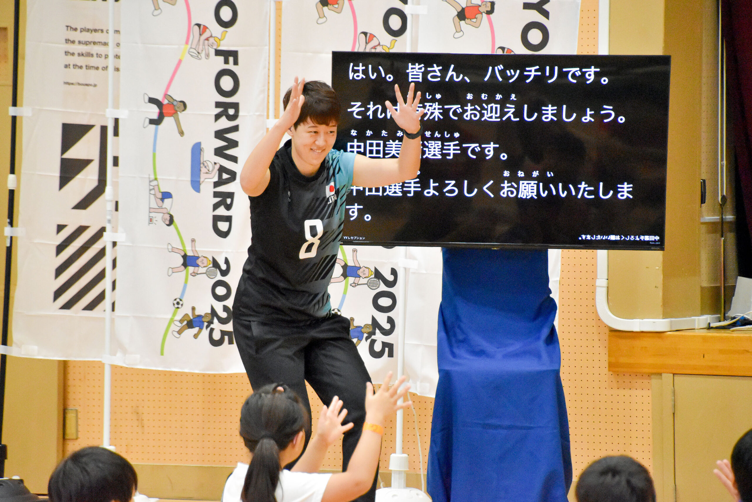 モニターの前で拍手の手話をする中田選手の写真