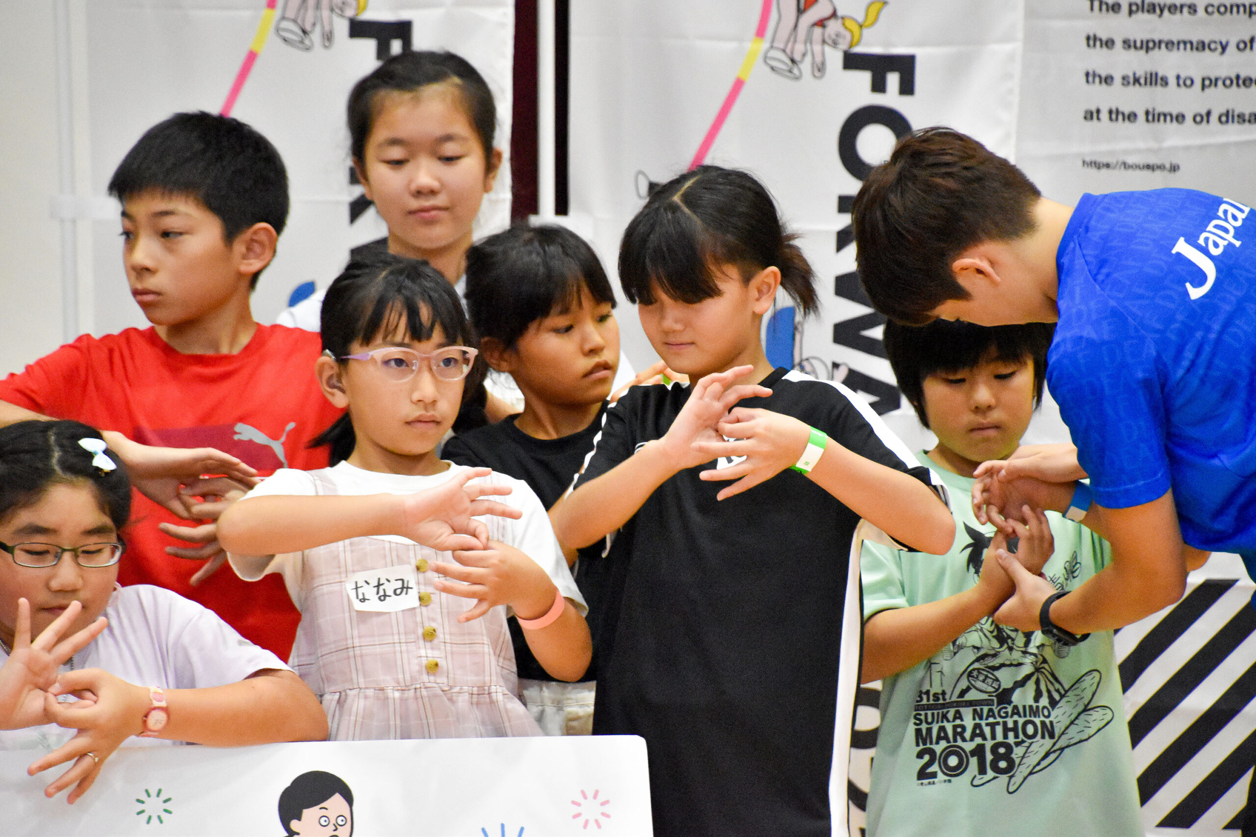 参加者の手を直してあげている中田選手と手話でデフリンピックを表している参加者の写真