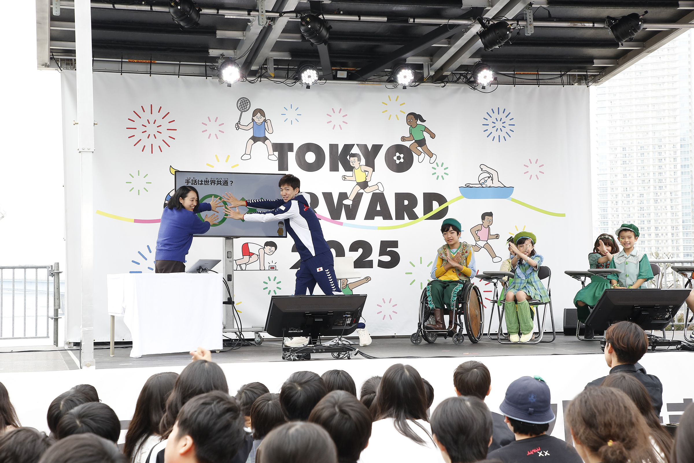 川俣さんと茨選手が壇上のモニターを腕で隠している写真