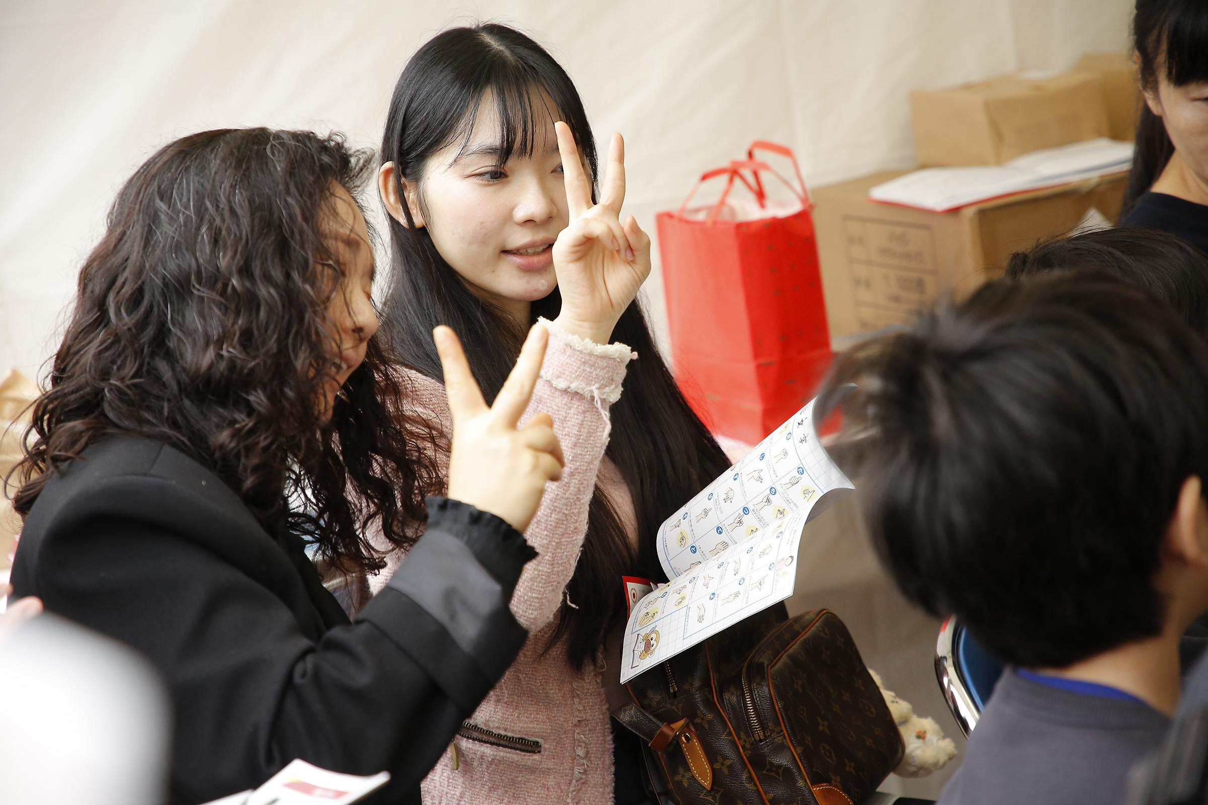 女性二人が冊子を見ながら2本の指を立てている写真