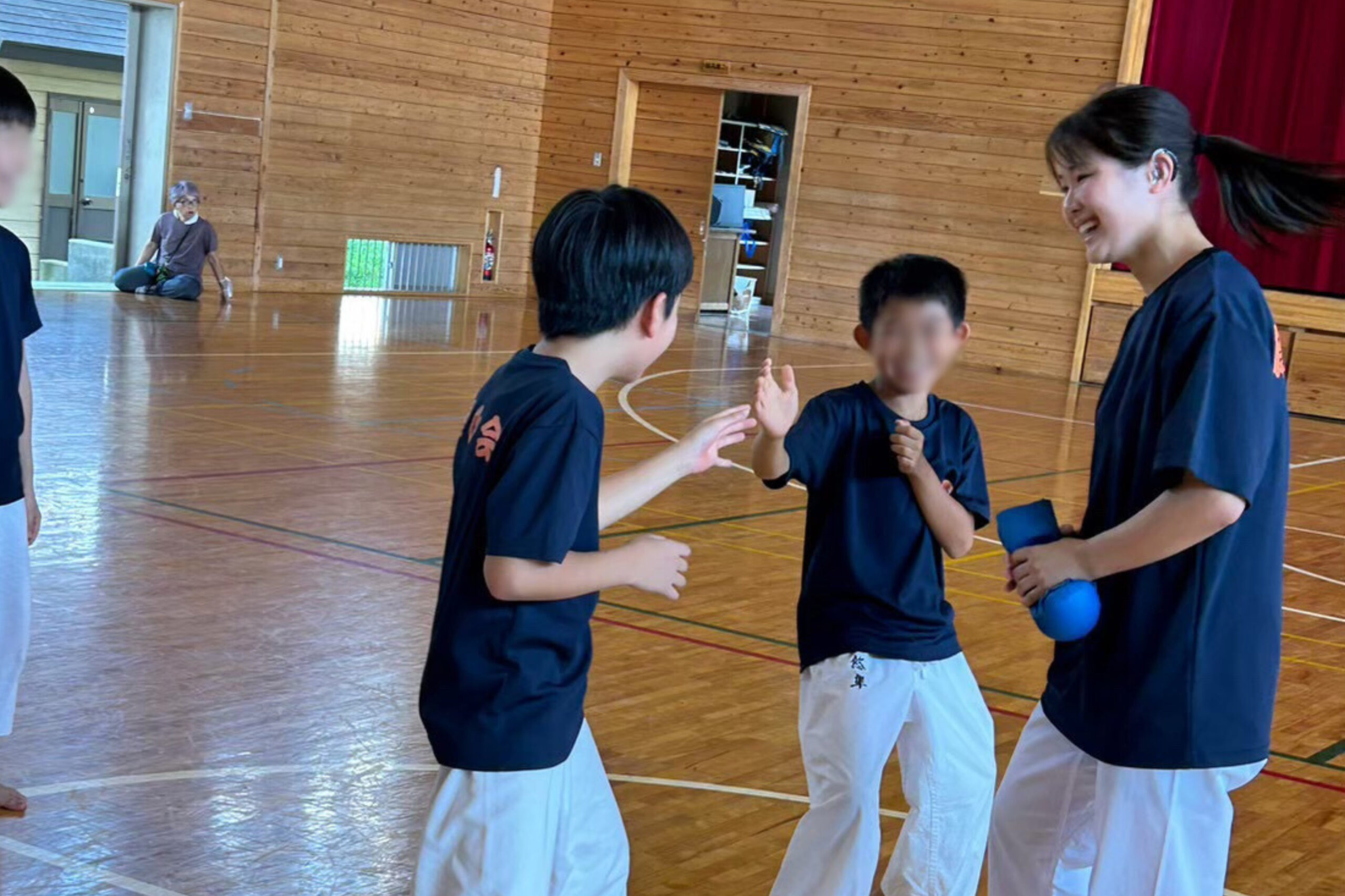 The photo of Ogura laughing with laughing children playing Kumite in the gymnasium.