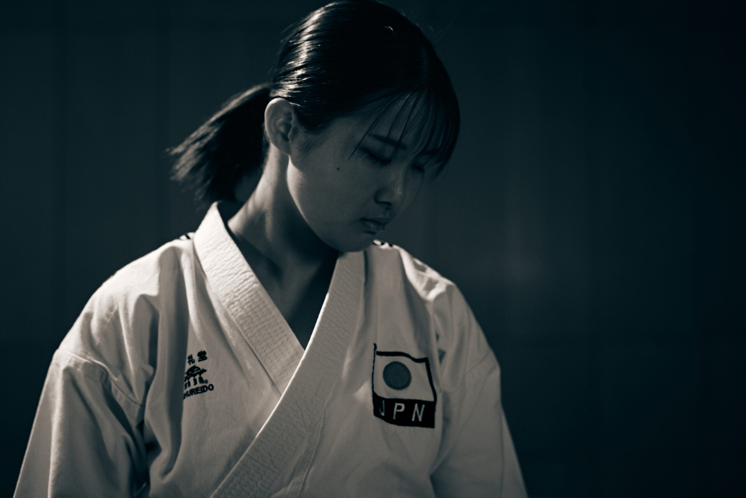 The black-and-white photo of Ogura in her karate uniform, looking down diagonally.
